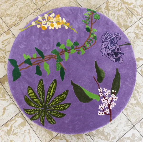 Photo taken from above, with light-colored tiles in the background. In the center is a circle of lilac-colored wool with patterns of flowers, bouquets, and colorful leaves.